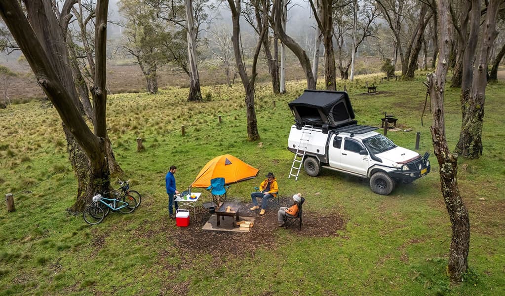 Campers around a wood barbecue next to a tent and a 4WD with a car tent in Polblue campground and picnic area. Credit: John Spencer/DCCEEW © DCCEEW