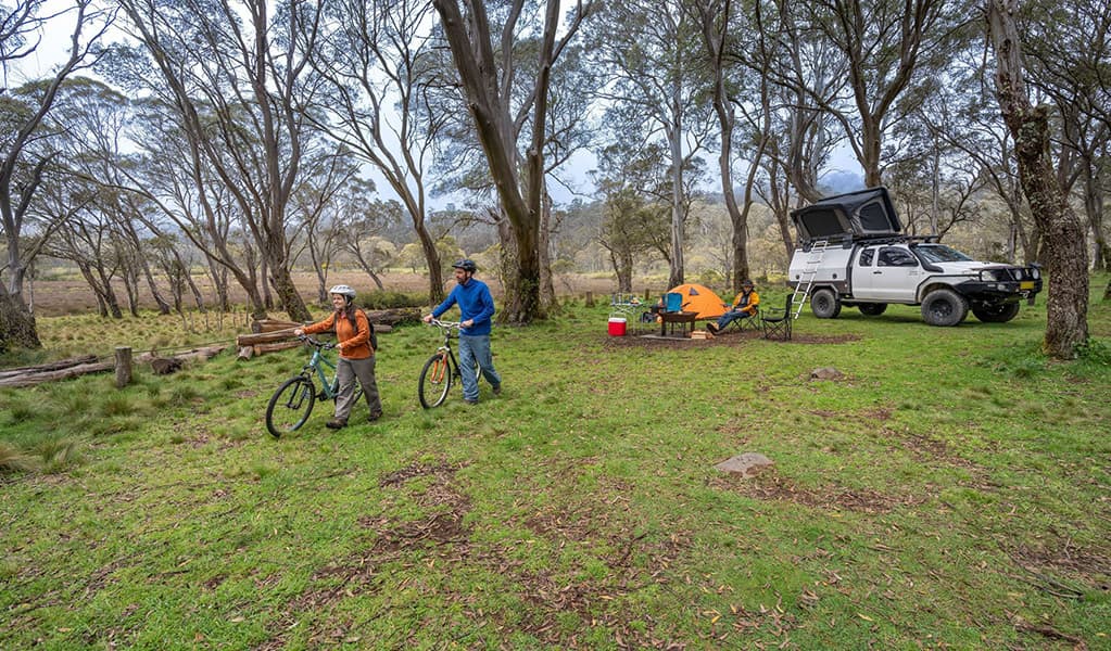 2 people walking mountain bikes from their campsite in Polblue campground and picnic area. Credit: John Spencer/DCCEEW © DCCEEW