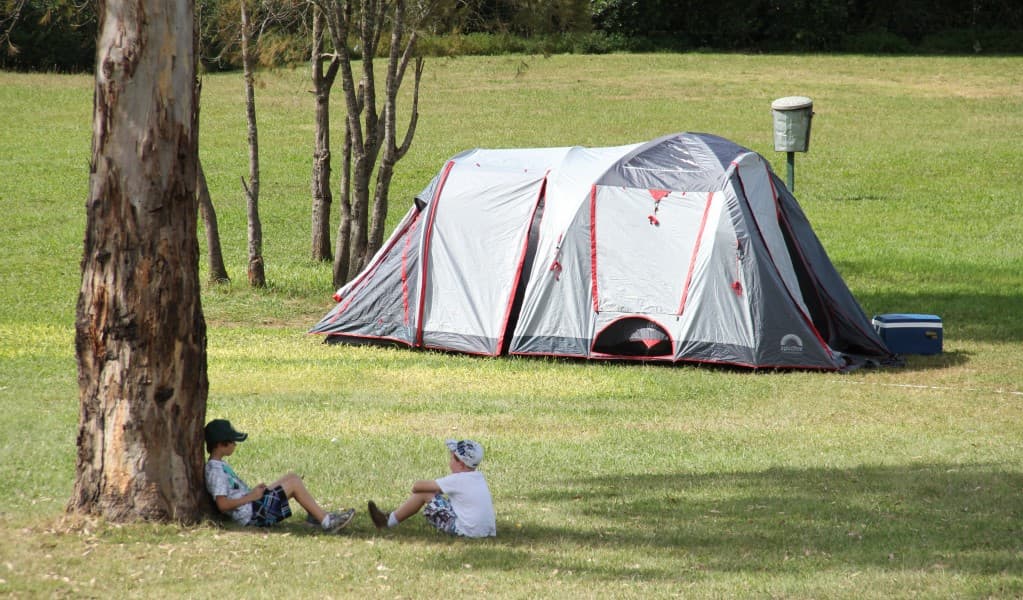 Children relaxing beneath a tree with their tent at Bents Basin campground