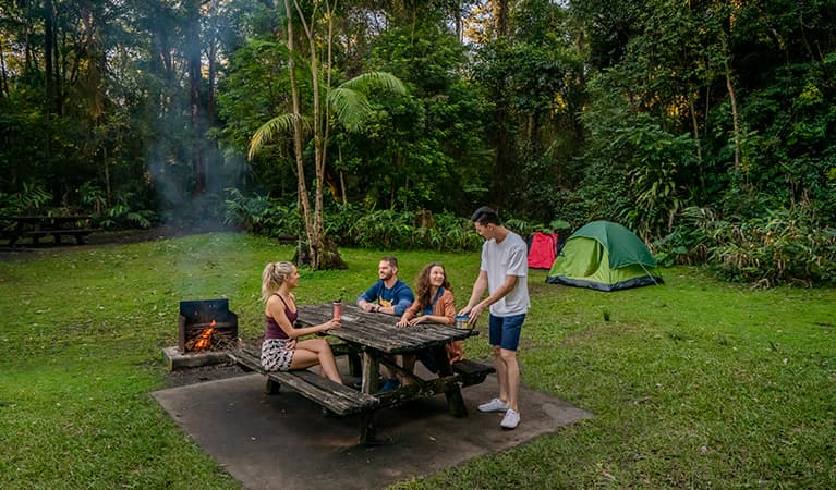 Four people sit at a picnic table beside a campfire at Sheepstation Creek campground, Border Ranges National Park. Photo credit: John Spencer © DPIE