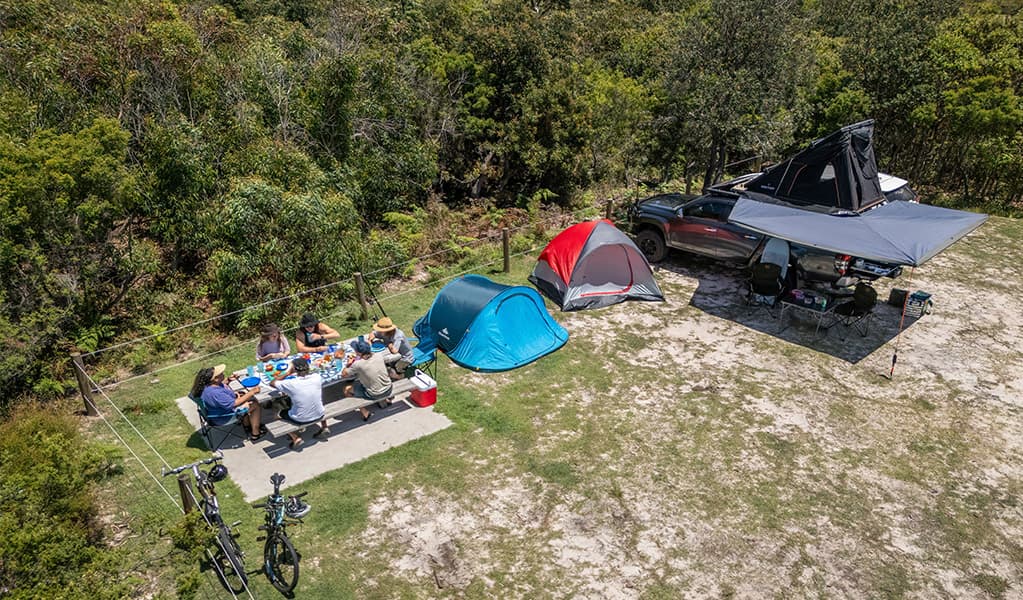 A group of campers eating at the picnic table on their campsite at Mibanbah-Black Rocks campground. Credit: John Spencer © DCCEEW