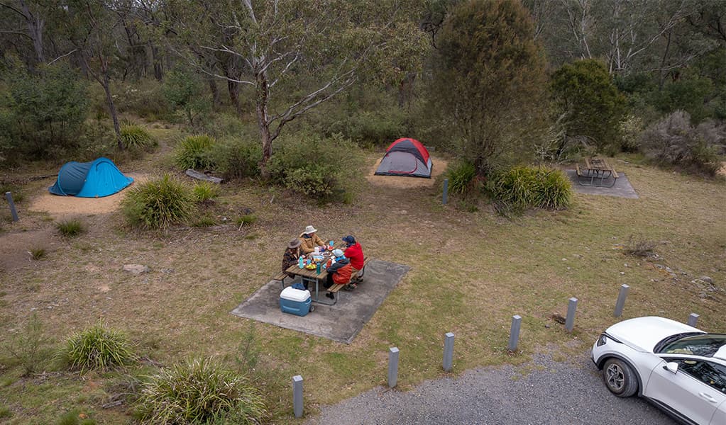 A group of campers eating at the picnic table next to their campsite at Bungonia campground. Photo: John Spencer/DCCEEW © DCCEEW