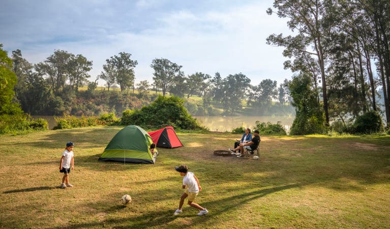 Parents sit outside their tent beside the Hawkesbury River while their kids play soccer, at Cattai campground in Cattai National Park. Photo: John Spencer/OEH