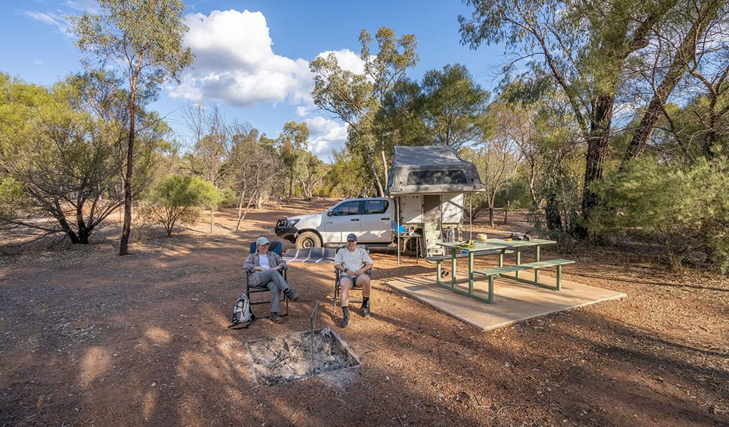 Two people sitting near picnic tables, a campfire and their tent and car at Woolshed Flat campground in Cocoparra National Park. Credit: Jonh Spencer © DCCEEW