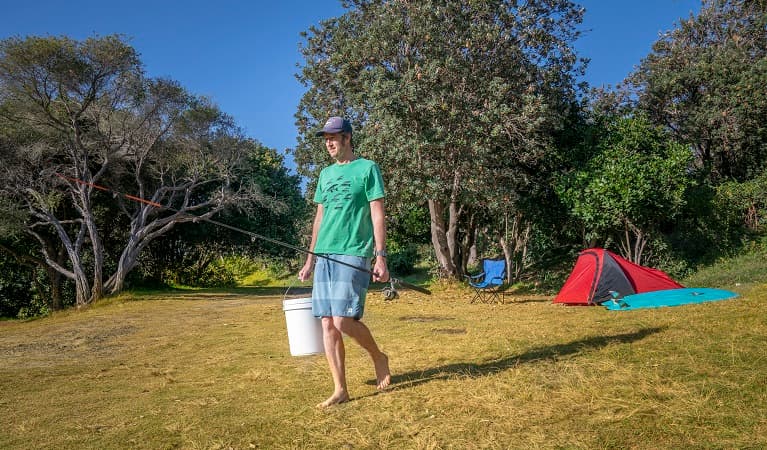 Camper with his fishing rod and bucket heading to the nearby beach, Goolawah National Park. Photo: John Spencer/OEH