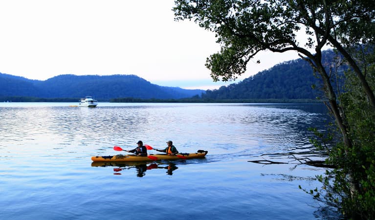 Hawkesbury River scene of 2 kayakers in a double kayak, with a river boat in the distance. Photo: Rosie Nicolai/DPIE