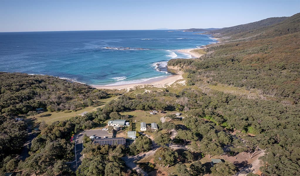 Aerial view of Pretty Beach campground and cabins, the ocean in the distance. Credit: John Spencer © DCCEEW