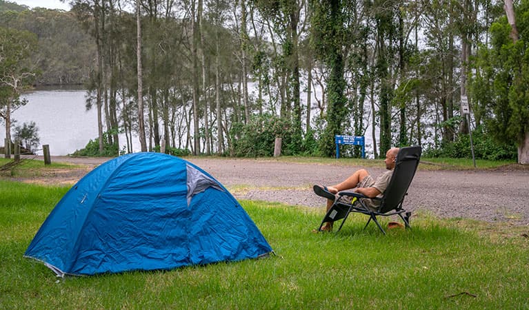 A man sitting by his tent at Violet Hill campground and picnic area in Myall Lakes National Park. Photo: John Spencer © DPIE