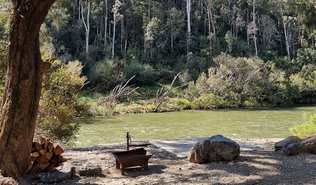 A campsite with a wood barbecue near the shore of the Nymboida River at Cod Hole campground and picnic area, Nymboi-Binderay National Park. Credit: Kit King © DCCEEW