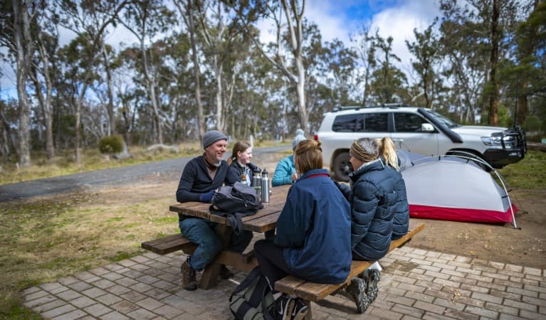 A group of friends sitting at a picnic table with their tent in the background at Dangars Gorge campground, Oxley Wild Rivers National Park. Photo: John Smith © DPE