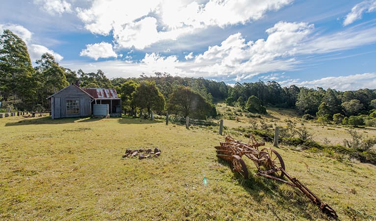 Alexanders Hut with old farm machinery in foreground and forest in background. Photo credit: John Spencer © DPIE