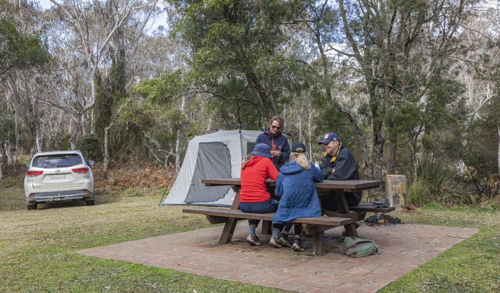 A group of friends at a picnic table next to their tent at Mooraback campground in Werrikimbe National Park. Photo: Josh Smith © DPE