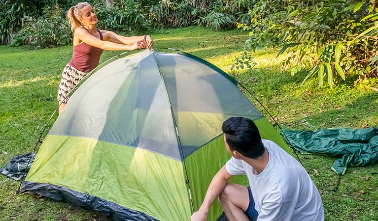 Illustrative NPWS camping image. 2 campers setting up a tent on the grass. Photo: John Spencer/DPIE