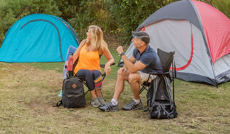 Illustrative NPWS camping image. 2 campers sitting with their backpacks with their tents set up in the background. Photo: John Spencer/DPIE